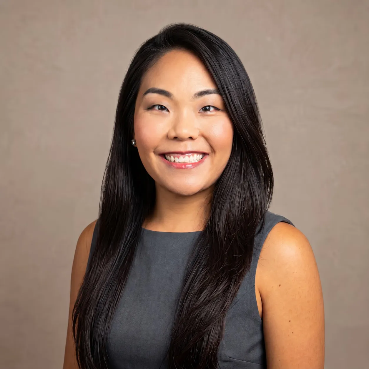 Dr. Annie Kim smiling in a charcoal sleeveless dress against a beige background.